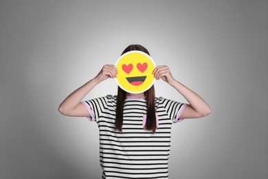 Woman covering face with heart eyes emoji on grey background