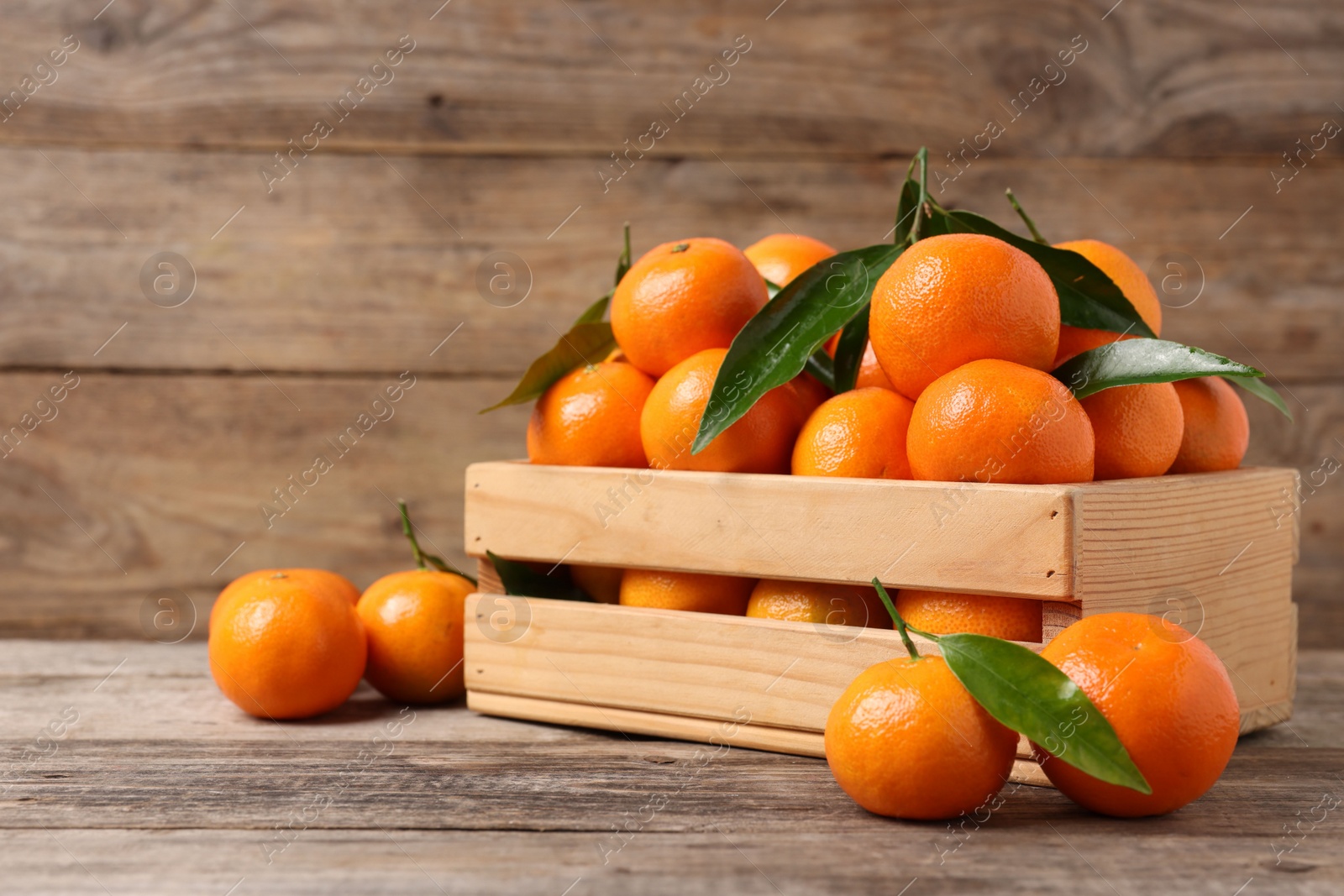 Photo of Delicious tangerines with leaves on wooden table. Space for text