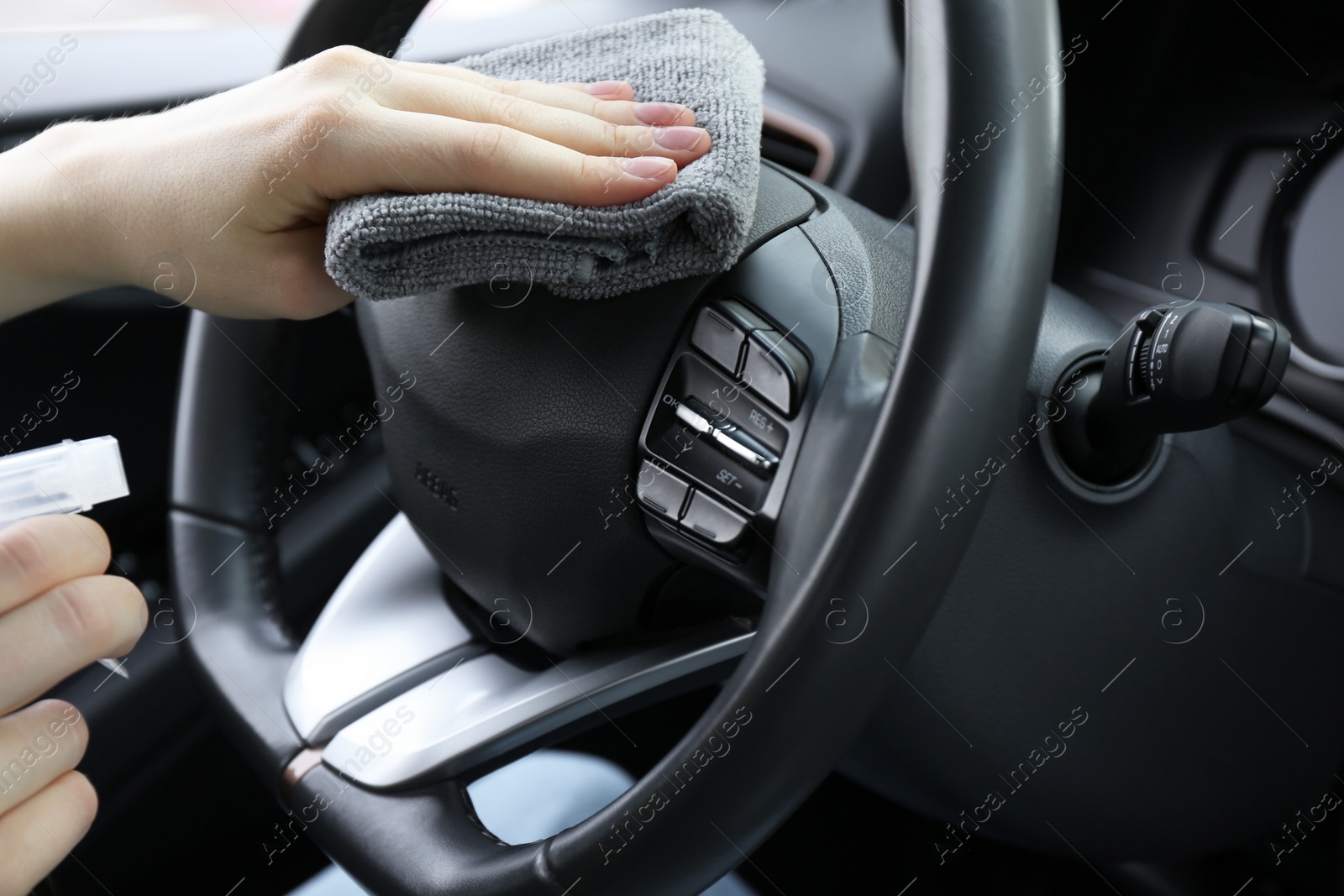 Photo of Woman cleaning steering wheel with rag in car, closeup