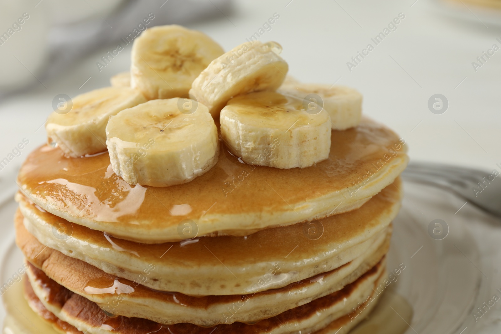 Photo of Delicious pancakes with bananas and honey on white table, closeup