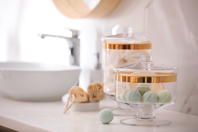 Photo of Jars with cotton pads and bath bombs on white countertop in bathroom