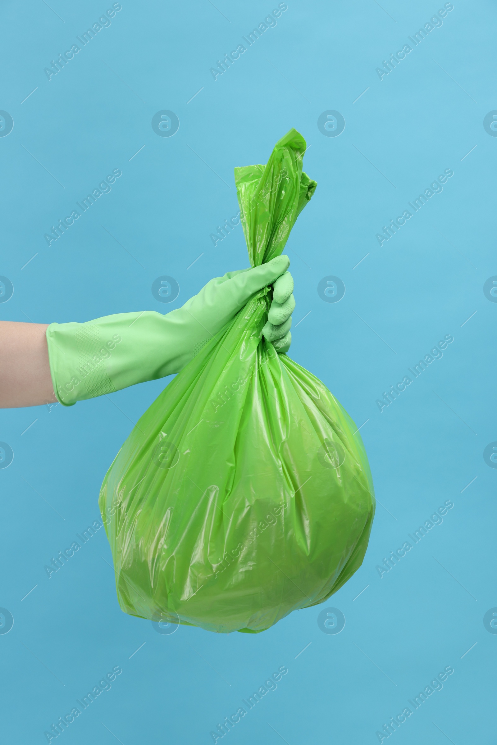 Photo of Woman holding plastic bag full of garbage on light blue background, closeup