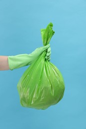 Photo of Woman holding plastic bag full of garbage on light blue background, closeup