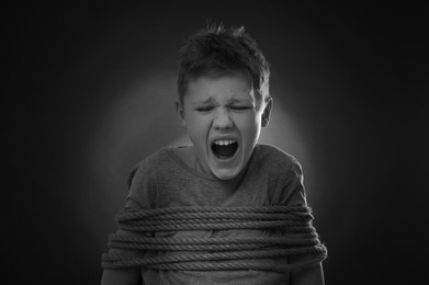 Scarred little boy tied up and taken hostage on dark background
