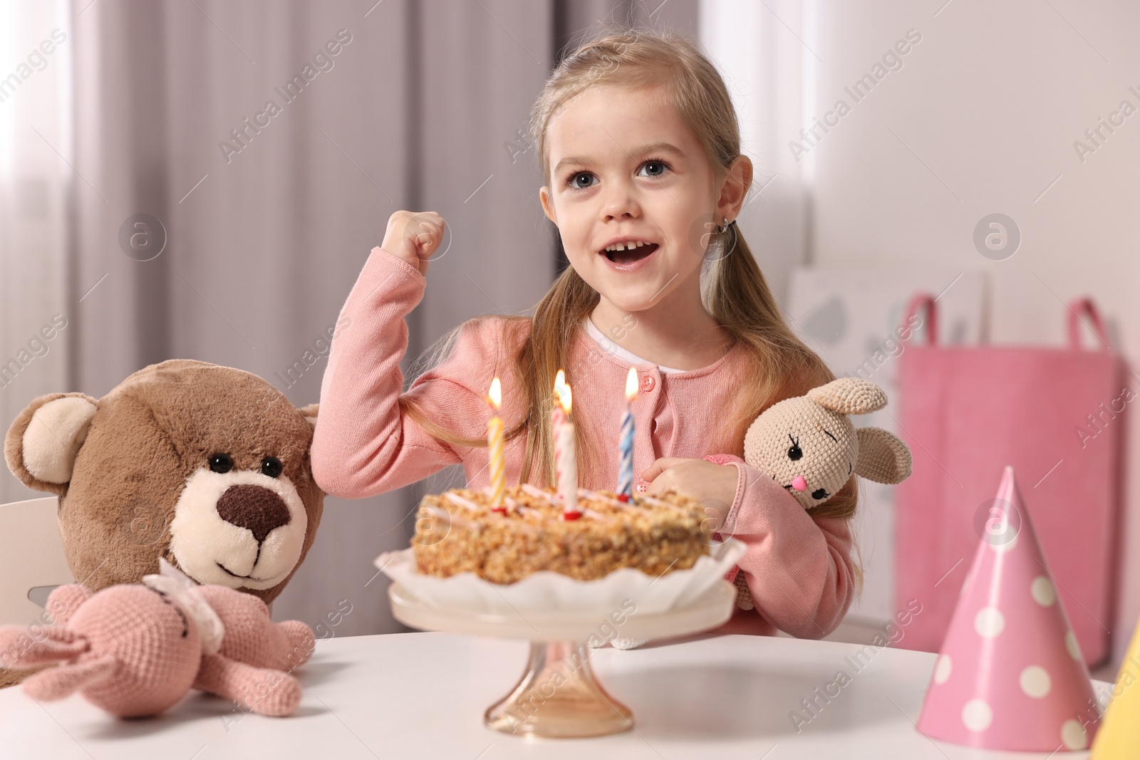 Photo of Cute girl with birthday cake and toys at table indoors