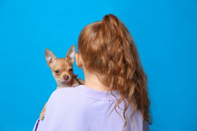 Little girl with her Chihuahua dog on light blue background, back view. Childhood pet