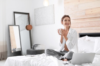 Photo of Young happy woman with cup of aromatic coffee on bed at home. Lazy morning