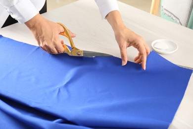 Seamstress cutting fabric at table in workshop, closeup