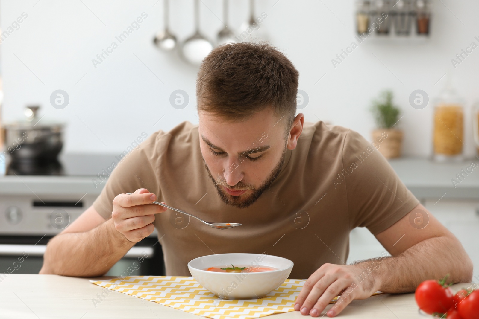 Photo of Young man eating tasty vegetable soup at table in kitchen