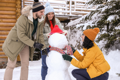 Happy friends making snowman outdoors. Winter vacation