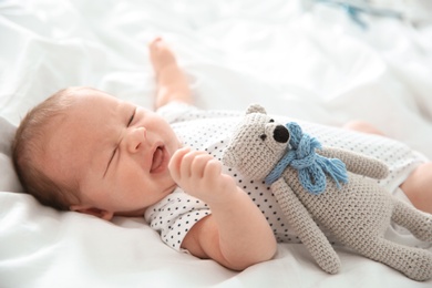 Adorable newborn baby with toy lying on bed sheet