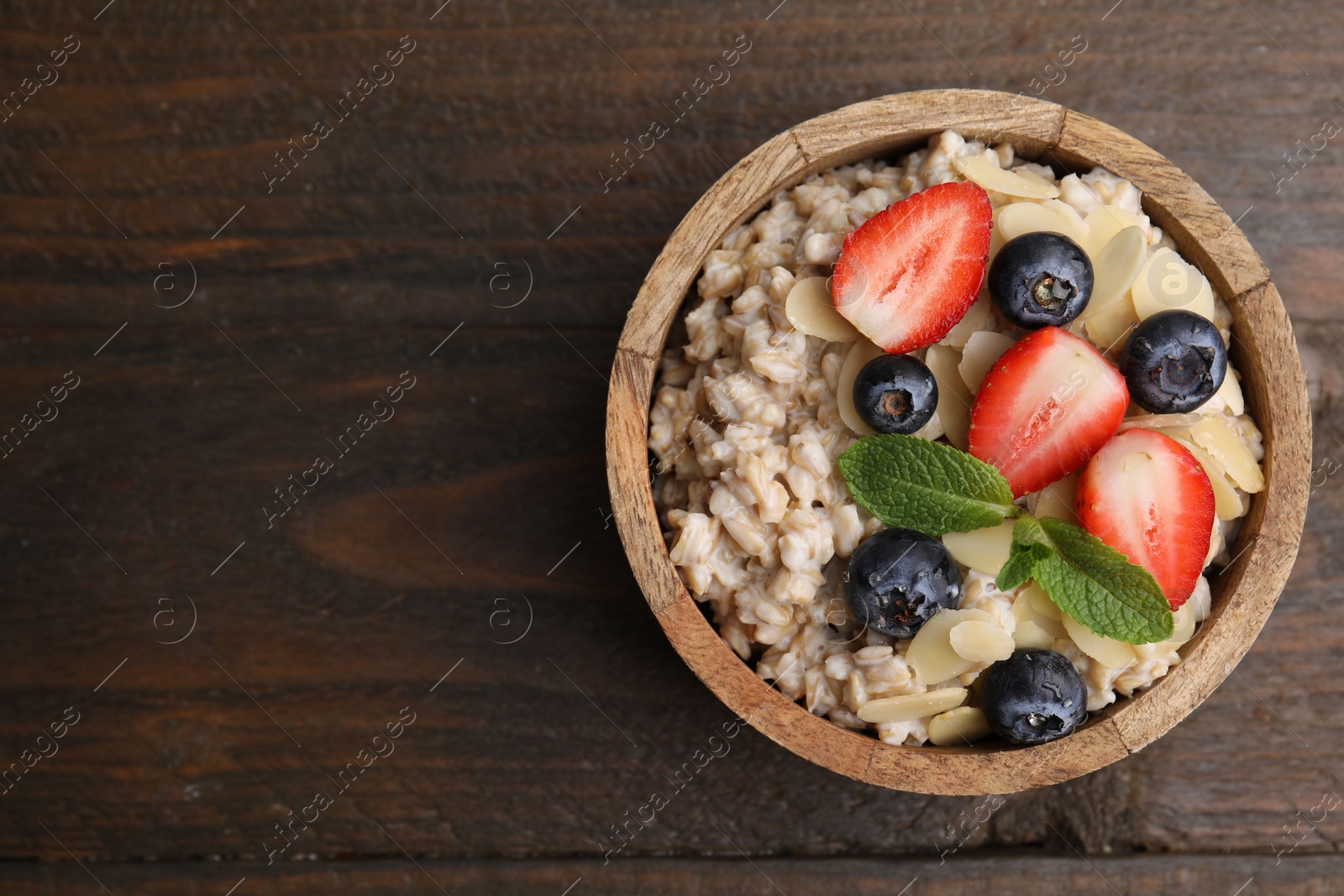 Photo of Tasty oatmeal with strawberries, blueberries and almond flakes in bowl on wooden table, top view. Space for text