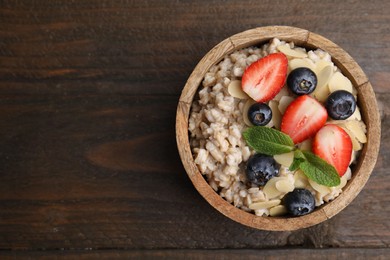 Photo of Tasty oatmeal with strawberries, blueberries and almond flakes in bowl on wooden table, top view. Space for text