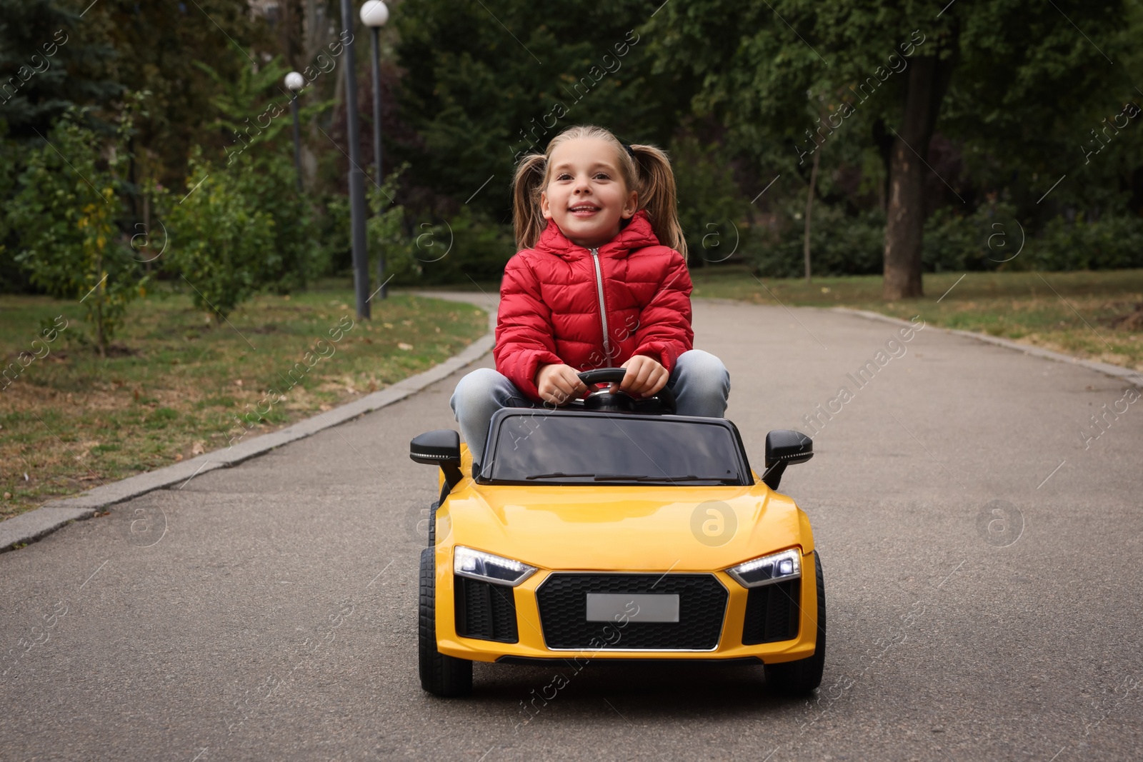 Photo of Cute little girl driving children's car outdoors