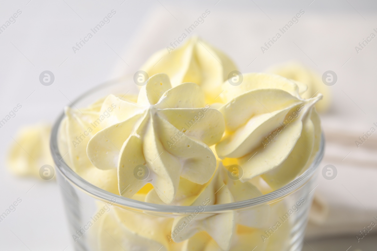 Photo of Tasty meringue cookies in glass on white table, closeup