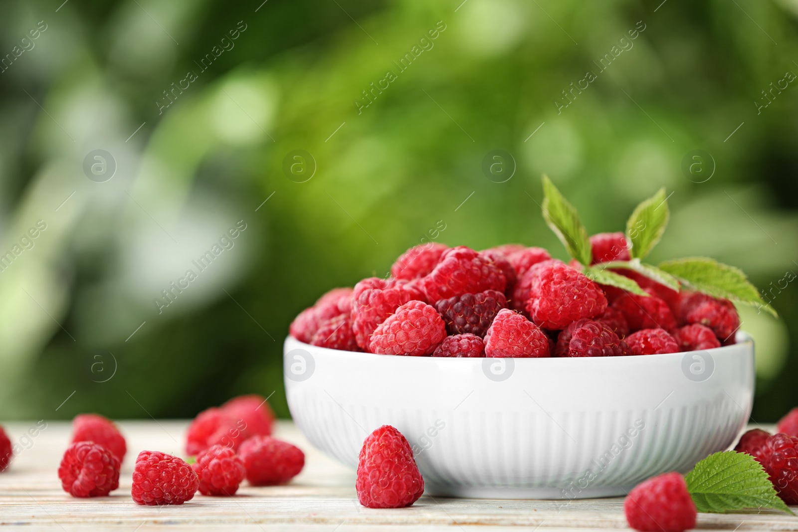 Photo of Bowl with delicious ripe raspberries on wooden table against blurred background, space for text