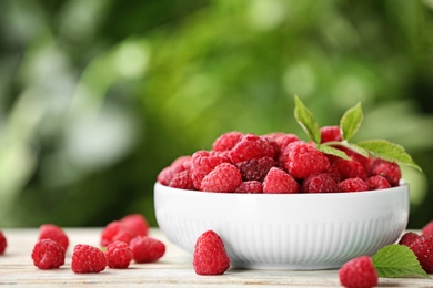 Photo of Bowl with delicious ripe raspberries on wooden table against blurred background, space for text