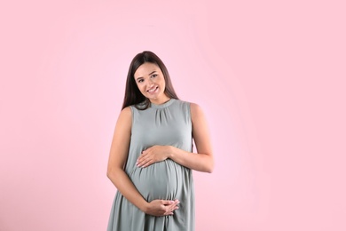 Beautiful pregnant woman holding hands on belly against color background