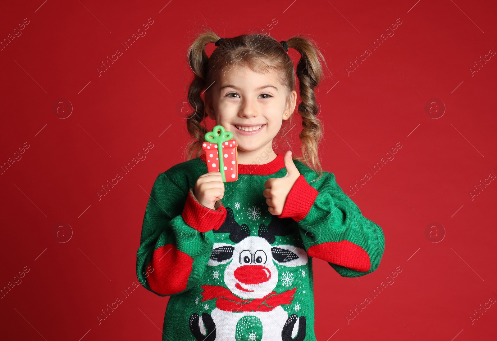 Photo of Cute little girl with Christmas gingerbread cookie on red background