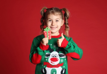 Cute little girl with Christmas gingerbread cookie on red background