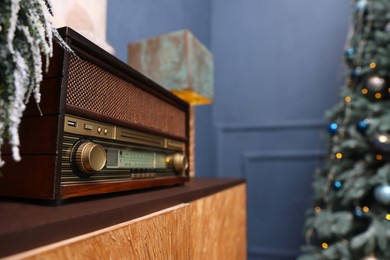Retro radio on wooden table and Christmas tree in room, space for text