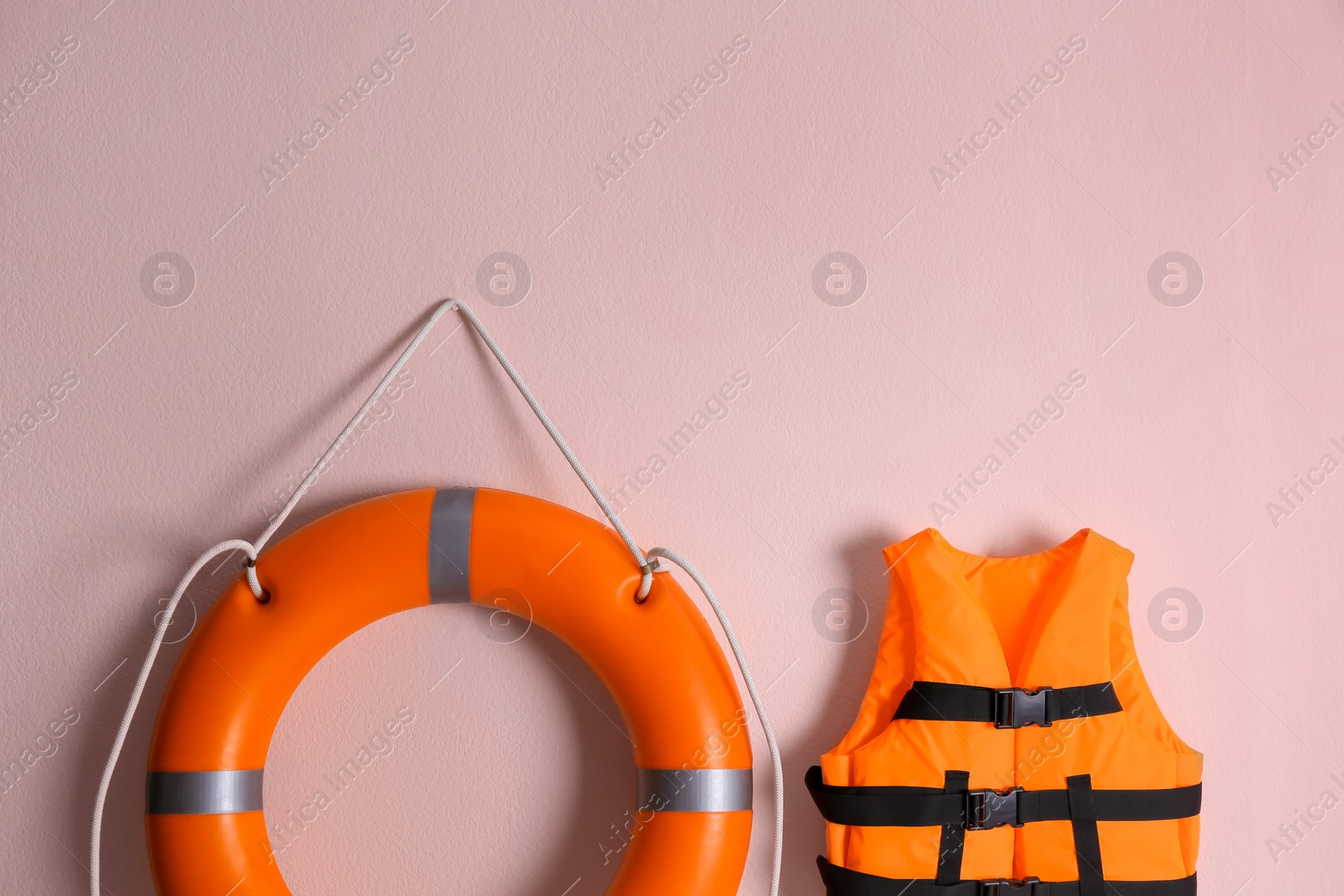 Photo of Orange life jacket and lifebuoy on pink background. Rescue equipment