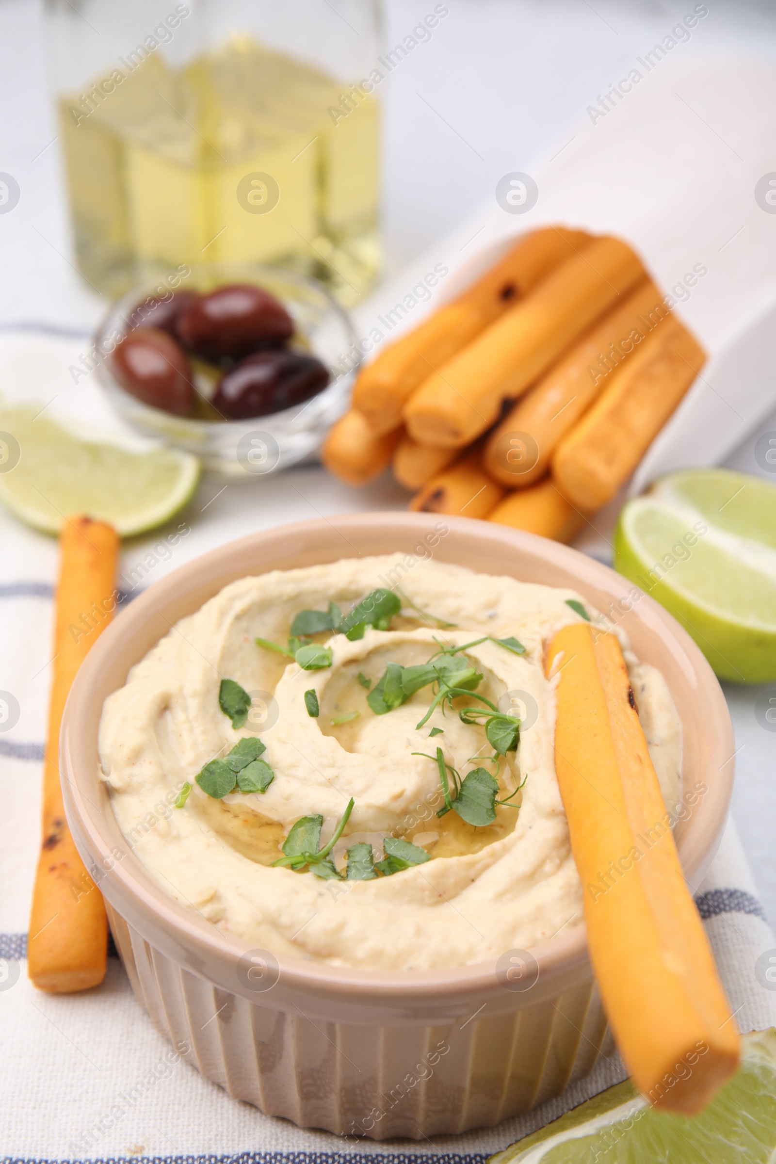 Photo of Delicious hummus with grissini sticks on light grey table, closeup