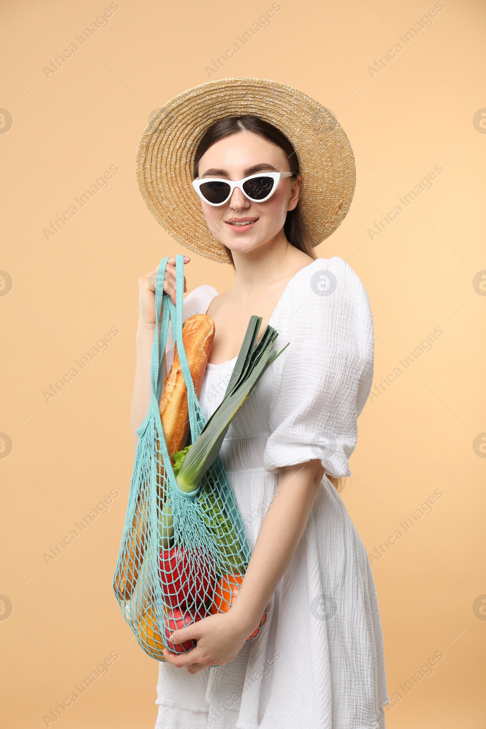 Photo of Woman with string bag of fresh vegetables and baguette on beige background