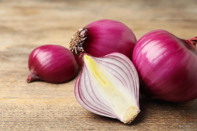 Ripe red onion bulbs on wooden table, closeup