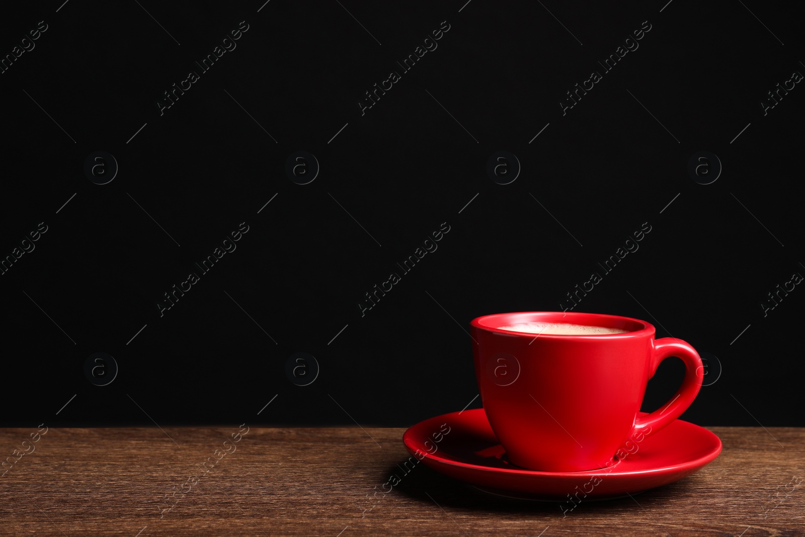 Photo of Red ceramic cup with hot aromatic coffee on wooden table against black background, space for text