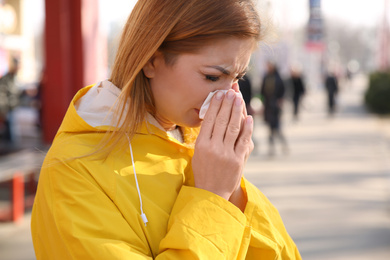 Photo of Sick woman sneezing on city street. Influenza virus