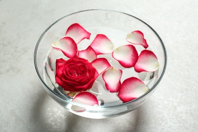 Photo of Glass bowl with aroma spa water, rose and petals on grey background