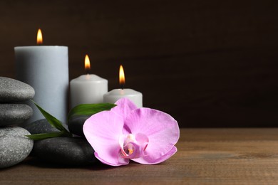 Photo of Spa stones, orchid flower, burning candles and bamboo sprout on wooden table. Space for text