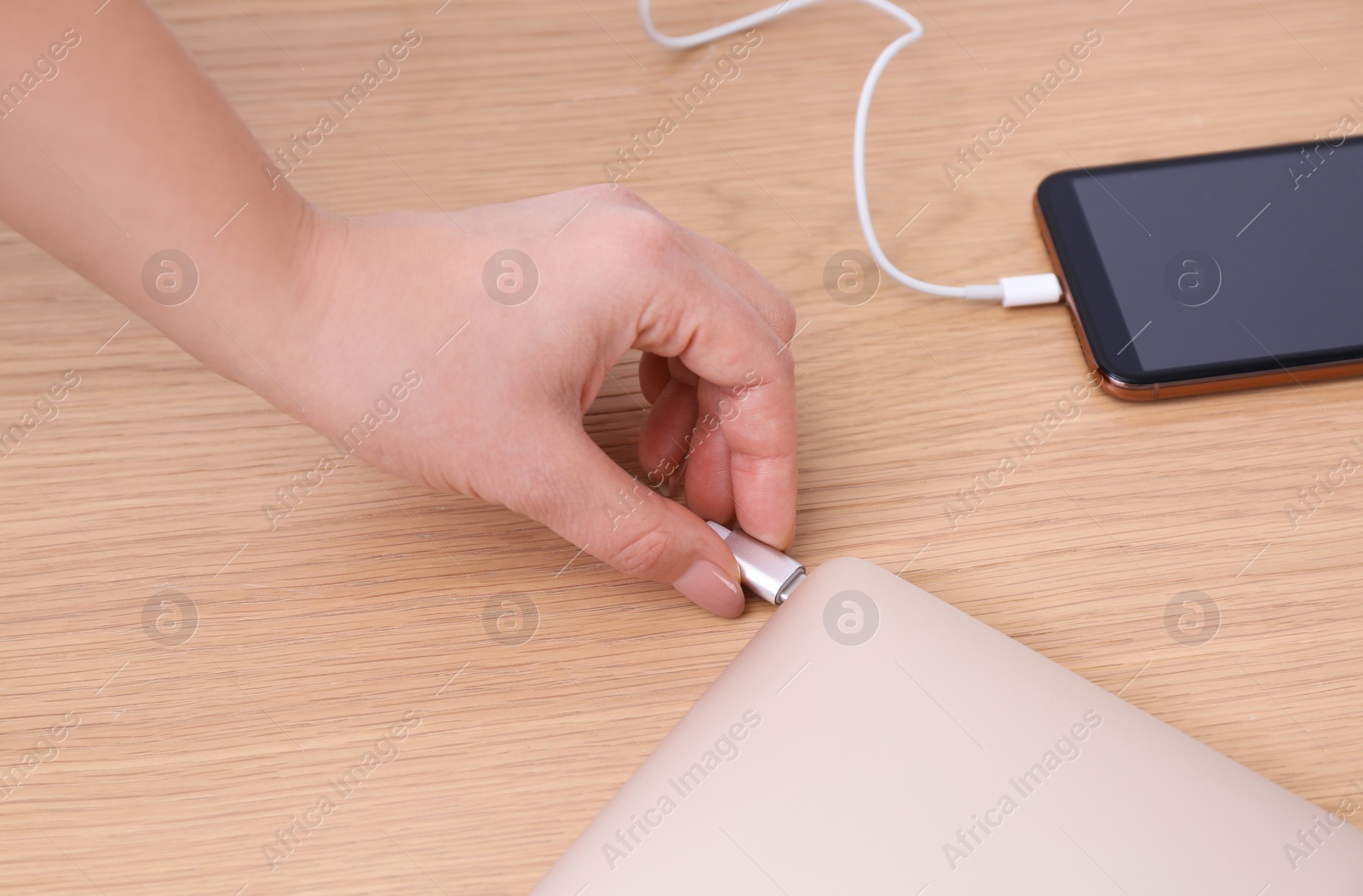 Photo of Woman connecting charging cable to laptop at wooden table, closeup