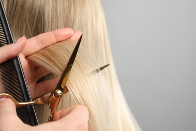 Photo of Hairdresser cutting client's hair with scissors on light grey background, closeup. Space for text