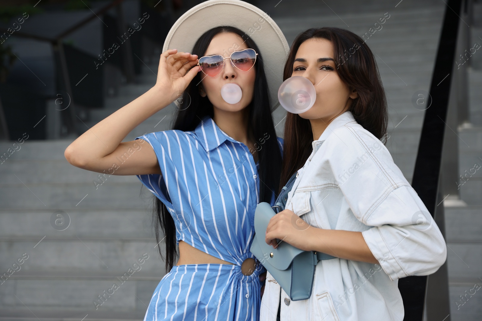 Photo of Beautiful stylish women blowing gums near stairs outdoors