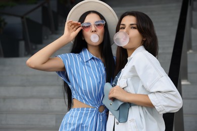 Beautiful stylish women blowing gums near stairs outdoors