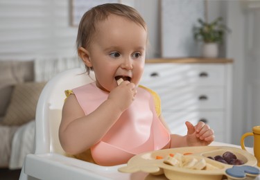 Photo of Cute little baby wearing bib while eating at home