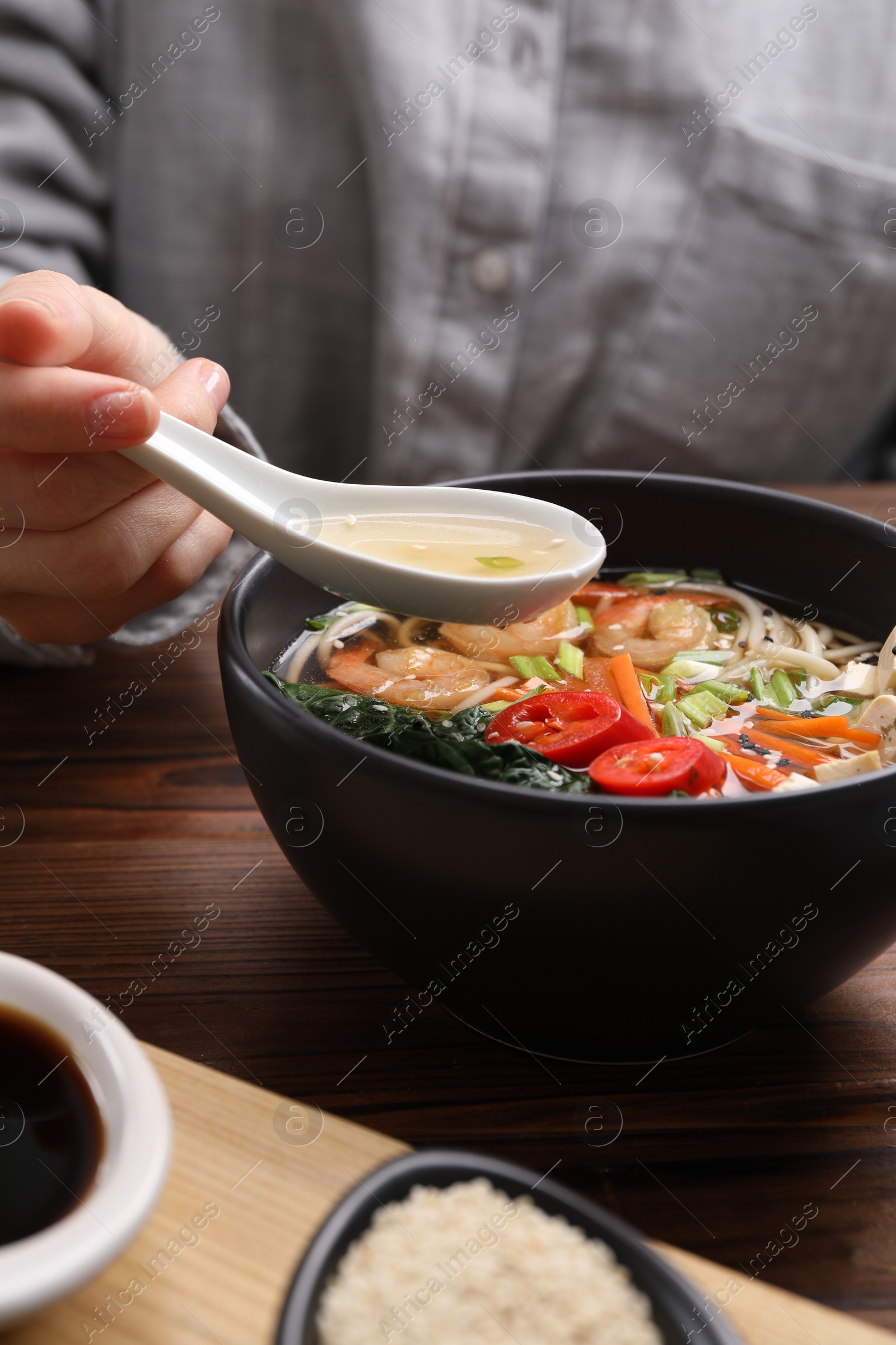 Photo of Woman eating delicious ramen with spoon at wooden table, closeup. Noodle soup