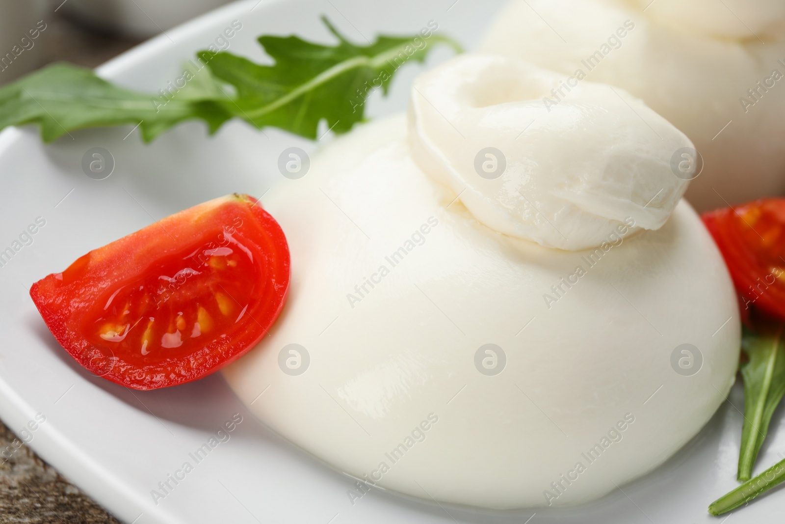 Photo of Delicious burrata cheese with arugula and tomato on wooden table, closeup