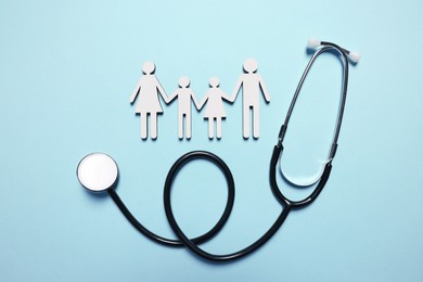 Figures of family near stethoscope on light blue background, flat lay. Insurance concept