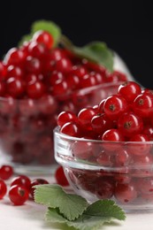 Photo of Many ripe red currants and leaves on white table, closeup