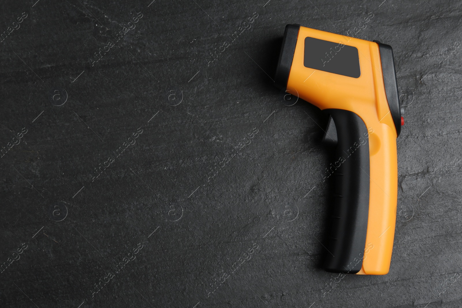 Photo of Modern non-contact infrared thermometer on black slate background, top view. Space for text