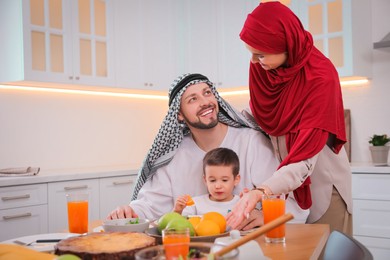 Happy Muslim family eating together in kitchen, space for text