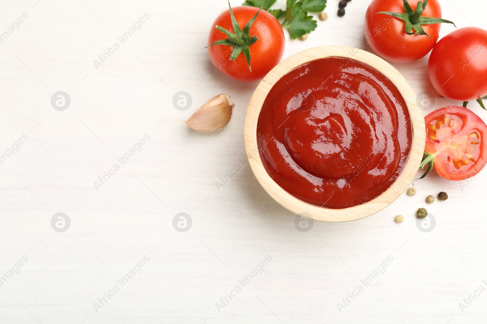 Photo of Delicious ketchup in bowl, peppercorns and tomatoes on white wooden table, flat lay. Space for text