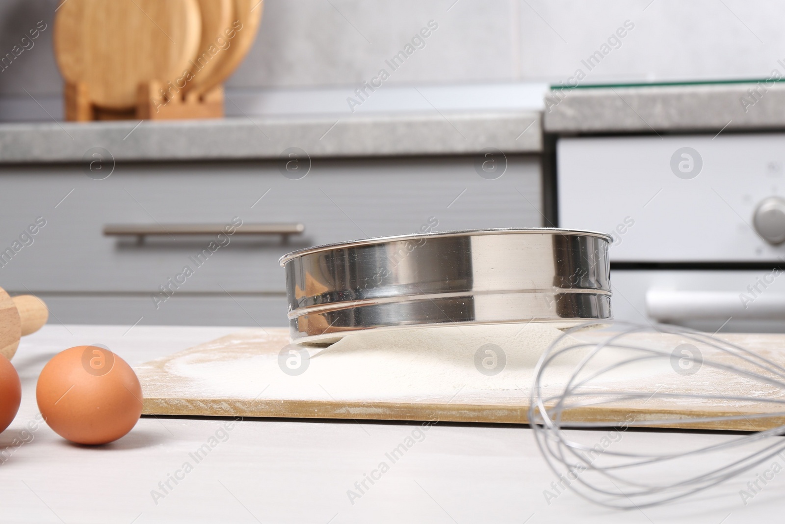 Photo of Sieve with flour, eggs, whisk and rolling pin on table in kitchen