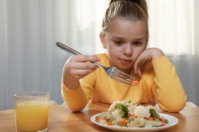 Photo of Cute little girl refusing to eat vegetable salad at home