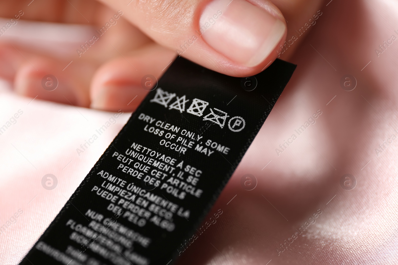 Photo of Woman reading clothing label with care symbols on pink silk shirt, closeup