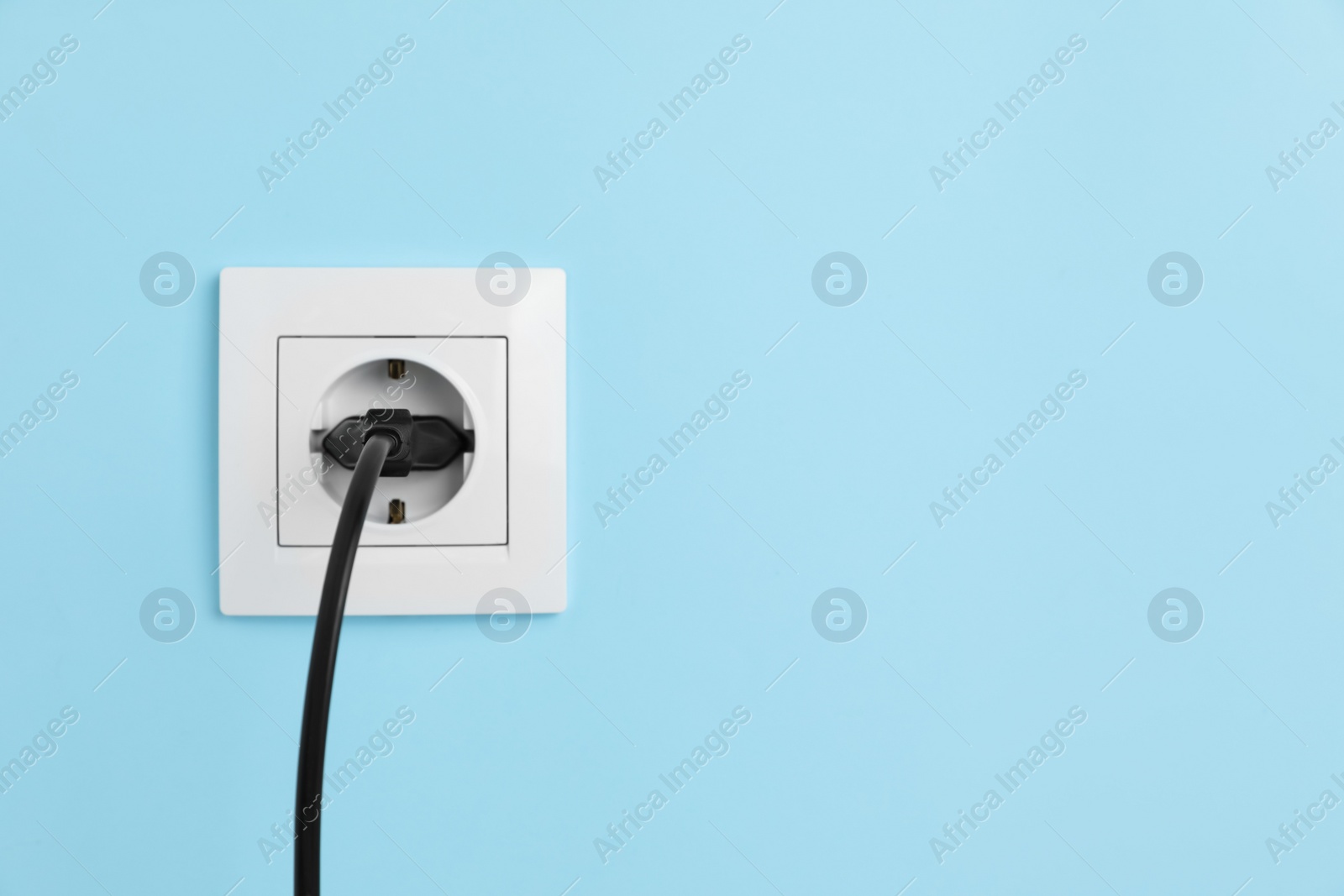 Photo of Power socket with inserted plug on light blue wall, space for text. Electrical supply