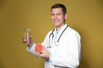 Nutritionist holding glass of pure water and ripe grapefruit on yellow background